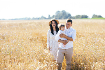 Happy family on a summer walk, mother, father and child walk in the wheat field and enjoy the beautiful nature, at sunset
