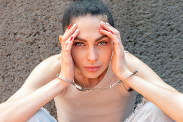 A young woman, 25-30 years old, is handcuffed against a gray wall, looking at the camera. Concept:...