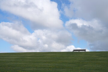 Sitzbank zur Erholung auf einem Deich, grüne Wiese bei schönen Wolken am Himmel, Nordsee