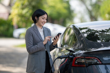 Progressive businesswoman using smartphone learning and check the charging time of electric car at charging station. Eco friendly rechargeable EV car concept.