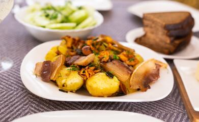 baked potatoes with chanterelles and bacon served with herbs and lightly salted cucumbers on table