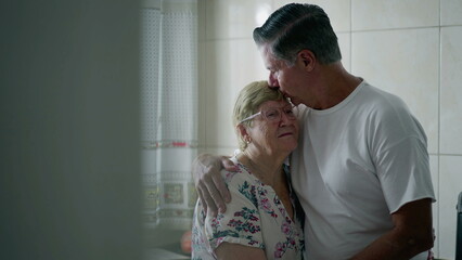Adult older son kissing elderly mother in forehead in candid loving affection at home. Real life...