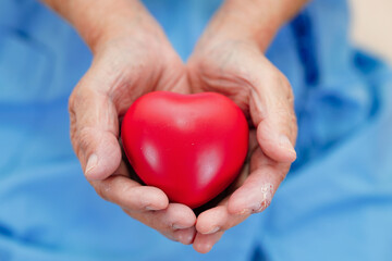 Asian elder senior woman patient holding red heart in hospital.