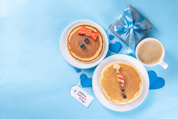 Father's day holiday idea, cute surprise gift. Child preparing breakfast for dad, creative decorated pancakes with tie, bow tie, inscription I love Dad. On light blue background, with child, dad hands