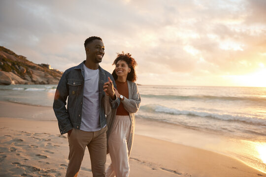Smiling young multiethnic couple walking along a beach at sunset
