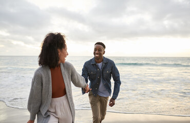 Smiling young multiethnic couple running hand in hand on a sandy beach - Powered by Adobe