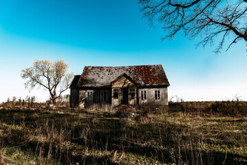 Fototapeta premium Abandoned 19th century house in a rural field at summer.Creepy summer evening.