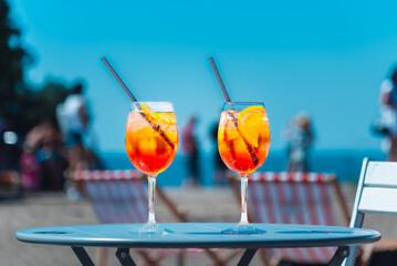 Two glasses of orange spritz aperol drink cocktail on table outdoors with sea and trees view...