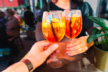 Couple celebratory toast with aperol spritz orange alcoholic cocktails at outdoors cocktail bar at...
