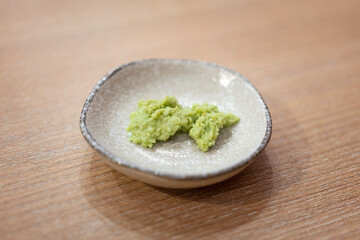 A bowl of wasabi, spicy dipping ingredient for Japanese food such as sashimi or sushi meal is placed on wooden table. Food and object photo.