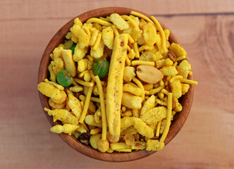 Delicious Khatta Meetha In wooden bowl and wooden background made with peanuts, sugar, raisins, and besan sev. Pile of Indian spicy snacks (Namkeen), top closeup.