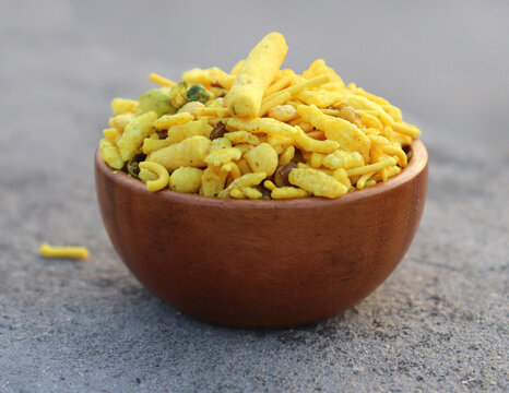 Delicious Khatta Meetha In wooden bowl and gray background, made with peanuts, sugar, raisins, and besan sev. Pile of Indian spicy snacks (Namkeen), top closeup.