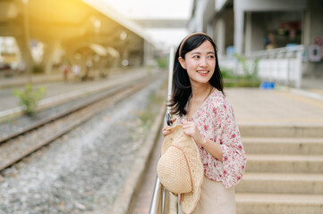 Obraz premium young asian woman traveler with weaving basket waiting for train in train station. Journey trip lifestyle, world travel explorer or Asia summer tourism concept.