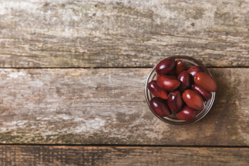 Red olives on a brown wooden background. Various types of olives in bowls and olive oil with fresh olive leaves. Copy space. Place for text. Mediterranean food. Vegan.