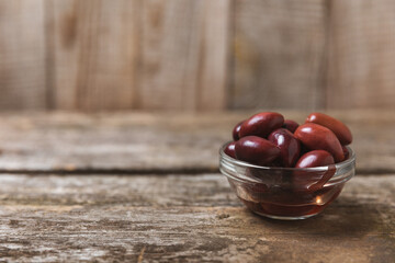 Red olives on a brown wooden background. Various types of olives in bowls and olive oil with fresh olive leaves. Copy space. Place for text. Mediterranean food. Vegan.