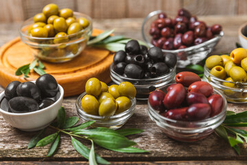 Green, black and red olives on a brown wooden background. Various types of olives in bowls and olive oil with fresh olive leaves. Copy space. Place for text. Mediterranean food. Vegan.