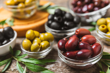 Green, black and red olives on a brown wooden background. Various types of olives in bowls and olive oil with fresh olive leaves. Copy space. Place for text. Mediterranean food. Vegan.