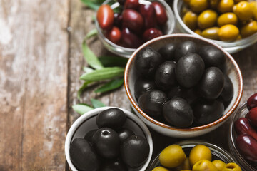 Green, black and red olives on a brown wooden background. Various types of olives in bowls and olive oil with fresh olive leaves. Copy space. Place for text. Mediterranean food. Vegan.