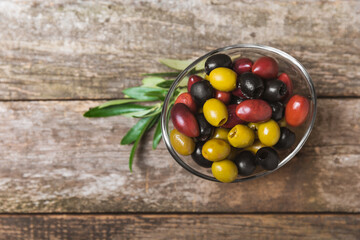 Green, black and red olives on a brown wooden background. Various types of olives in bowls and olive oil with fresh olive leaves. Copy space. Place for text. Mediterranean food. Vegan.