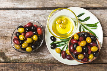 Green, black and red olives on a brown wooden background. Various types of olives in bowls and olive oil with fresh olive leaves. Copy space. Place for text. Mediterranean food. Vegan.