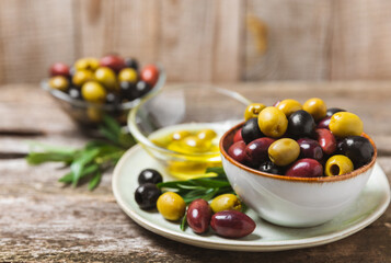 Green, black and red olives on a brown wooden background. Various types of olives in bowls and olive oil with fresh olive leaves. Copy space. Place for text. Mediterranean food. Vegan.