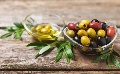 Foto op Plexiglas Green, black and red olives on a brown wooden background. Various types of olives in bowls and olive oil with fresh olive leaves. Copy space. Place for text. Mediterranean food. Vegan. © Avocado_studio