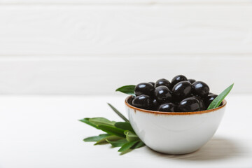 Black olives on a white wooden background. Various types of olives in bowls and olive oil with fresh olive leaves. Copy space. Place for text. Mediterranean food. Vegan.