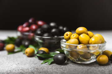 Green, black and red olives on a textured marble background. Various types of olives in bowls and olive oil with fresh olive leaves. Copy space. Place for text. Mediterranean food. Vegan.