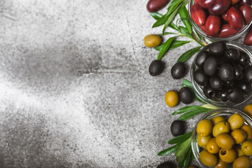 Green, black and red olives on a textured marble background. Various types of olives in bowls and olive oil with fresh olive leaves. Copy space. Place for text. Mediterranean food. Vegan.