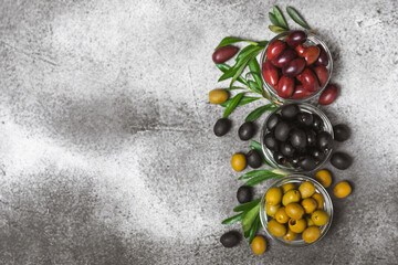 Green, black and red olives on a textured marble background. Various types of olives in bowls and olive oil with fresh olive leaves. Copy space. Place for text. Mediterranean food. Vegan.