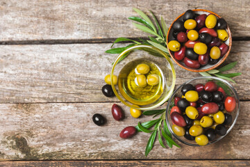 Green, black and red olives on a brown wooden background. Various types of olives in bowls and olive oil with fresh olive leaves. Copy space. Place for text. Mediterranean food. Vegan.