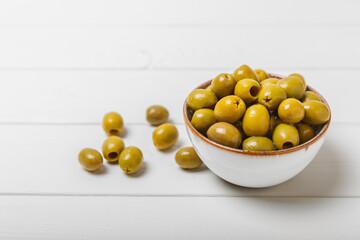 Green olives on a white wooden background. Various types of olives in bowls and olive oil with fresh olive leaves. Copy space. Place for text. Mediterranean food. Vegan.