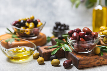 Green, black and red olives on a textured marble background. Various types of olives in bowls and olive oil with fresh olive leaves. Copy space. Place for text. Mediterranean food. Vegan.