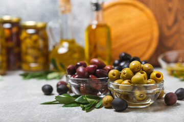 Green, black and red olives on a textured marble background. Various types of olives in bowls and olive oil with fresh olive leaves. Copy space. Place for text. Mediterranean food. Vegan.