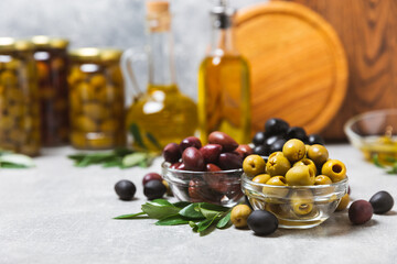 Green, black and red olives on a textured marble background. Various types of olives in bowls and...