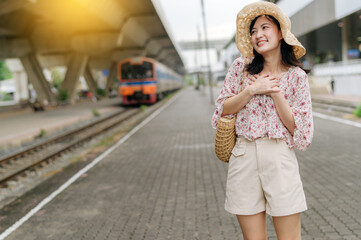 young asian woman traveler with weaving basket happy smiling and looking to a camera beside train coming background. Journey trip lifestyle, world travel explorer or Asia summer tourism concept.