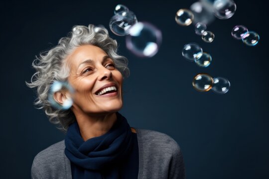 Headshot portrait photography of a happy mature woman blowing bubbles against a navy blue background. With generative AI technology