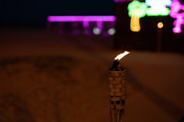 A burning torch at night on the beach against the backdrop of a bar close-up.