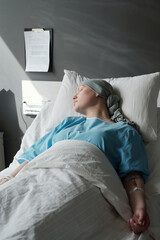 Young woman in headscarf and blue shirt lying in bed in clinics and sleeping during medical...