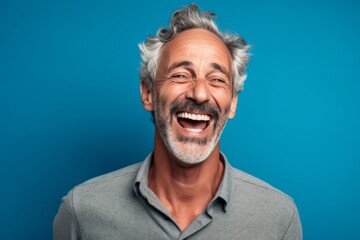Close-up portrait photography of a grinning mature man placing the hand over the mouth in a laughter gesture against a soft blue background. With generative AI technology