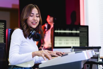 Asian producer woman in white shirt playing piano in sound studio with warm lighting background, Happy female music composer artist.