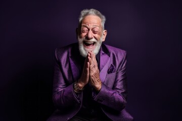 Fototapeta premium Lifestyle portrait photography of a joyful old man placing the hand over the mouth in a laughter gesture against a deep purple background. With generative AI technology