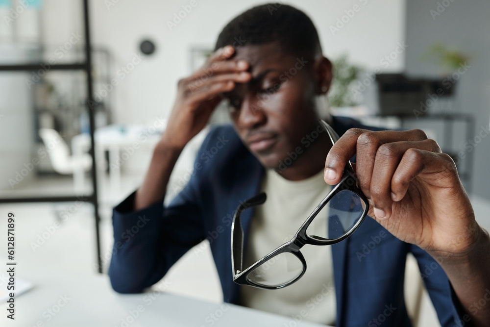 Poster hand of young pensive analyst in formalwear holding eyeglasses and keeping palm on forehead while wo