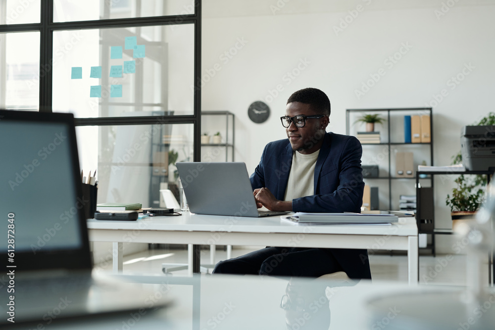 Poster young confident broker in formalwear looking through online data on laptop screen while preparing ne