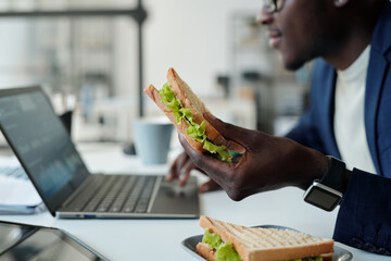 Focus on appetizing vegetarian sandwich in hand of young hungry African American manager in...