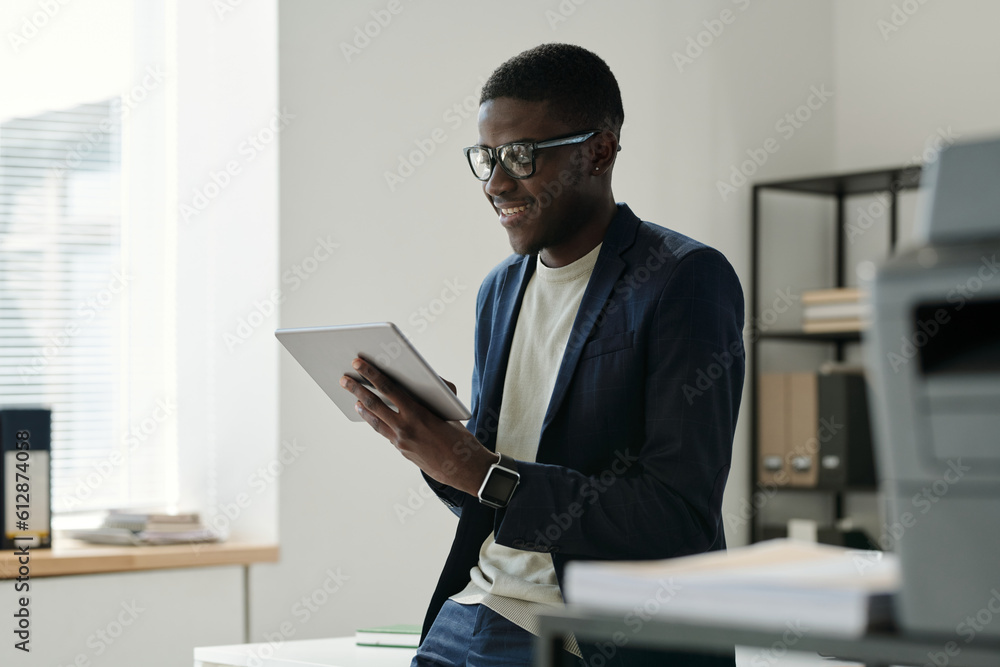 Aufkleber young african american businessman in formalwear using tablet while standing by workplace in office 