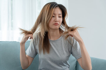 Asian woman very sad and upset looking at damaged hair, hair loss, hair thinning problem, vitamin...