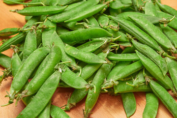 Fototapeta premium green ripe plucked pea pods on a wooden kitchen cutting board close-up