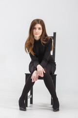 girl model in black tight-fitting dress sits on chair in studio on white background