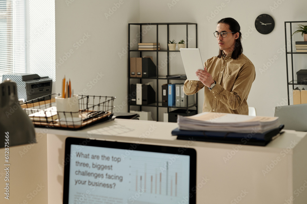 Poster young serious businessman looking tablet screen during communication with colleague in video chat or